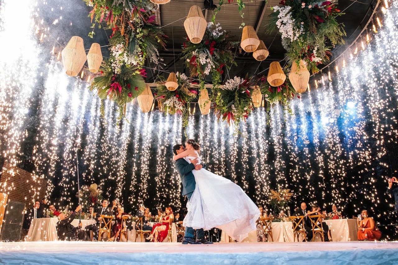 Pareja bailando su primer baile bajo cortina de chispas frías voladas en boda