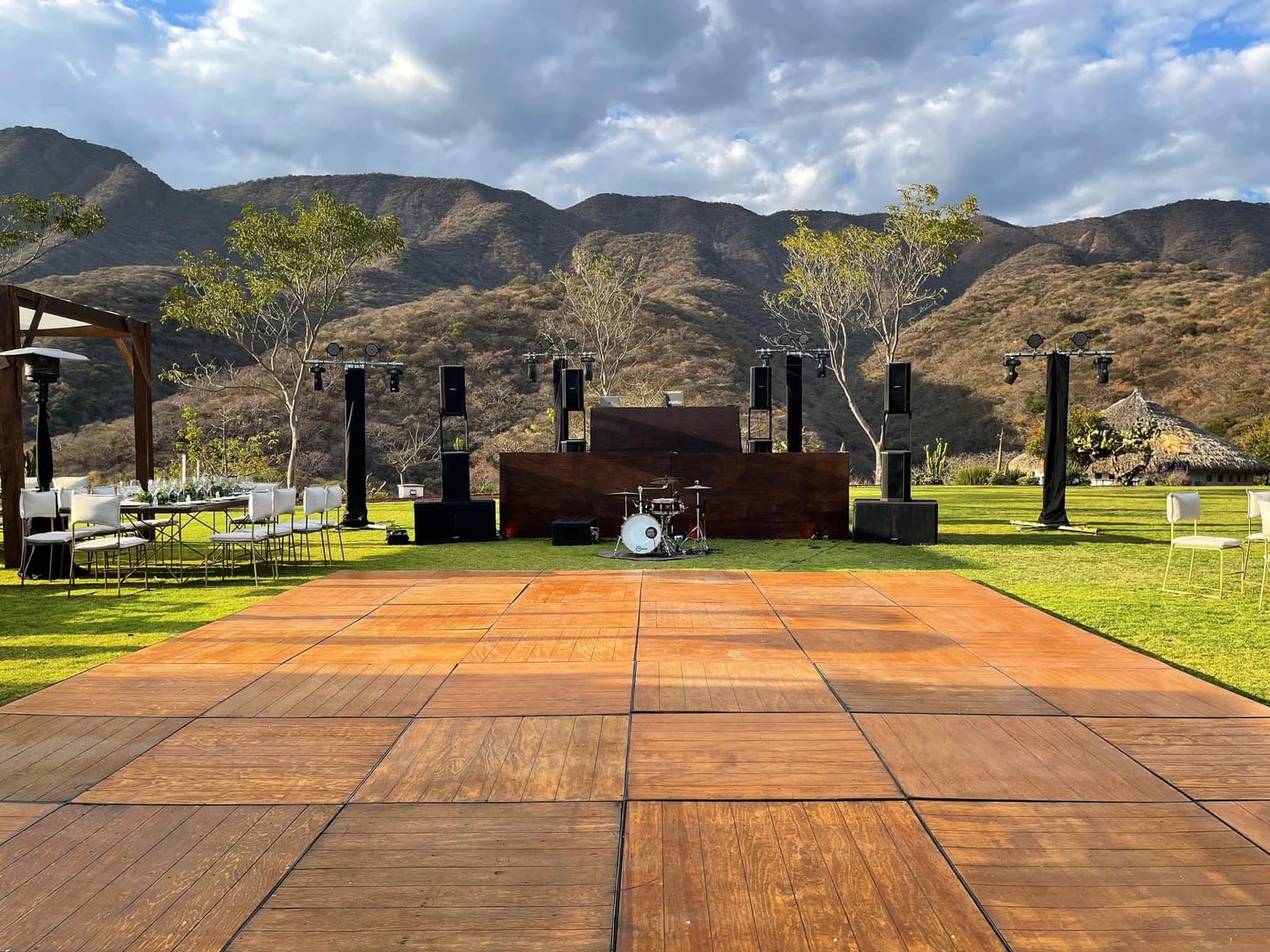 Escenario exterior con torres de audio line array y pista de duela frente a las montañas