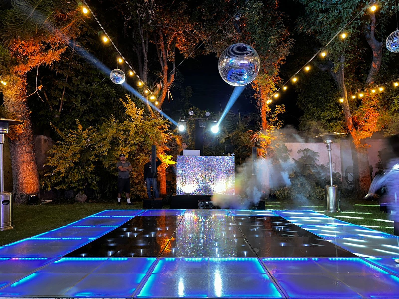 Esfera disco y haces de luz sobre pista de baile azul en jardín