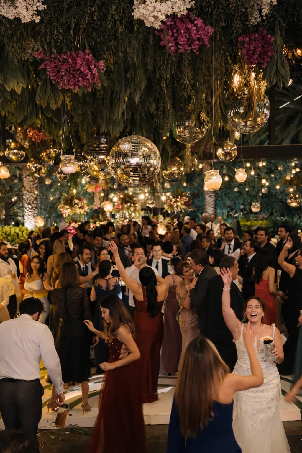 Fiesta en jardín bajo dosel floral con esferas disco y manos arriba
