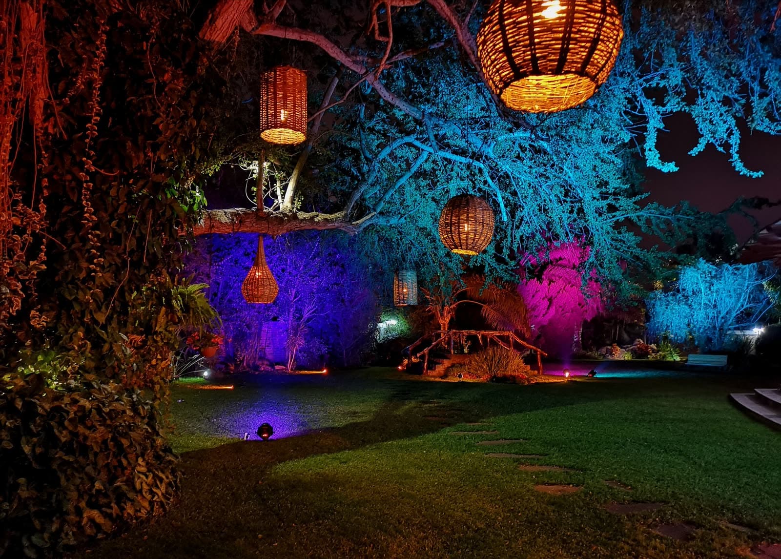 Jardín nocturno iluminado con linternas y luz de color entre los árboles