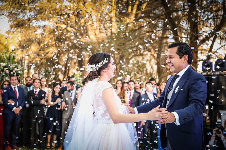 Novios riendo tomados de las manos bajo lluvia de confeti en boda de jardín de día