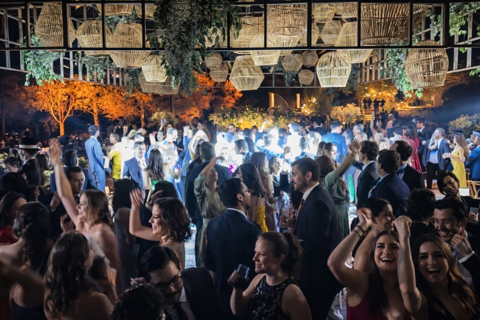 Pista de baile llena de invitados bailando en boda de jardín con luces cálidas