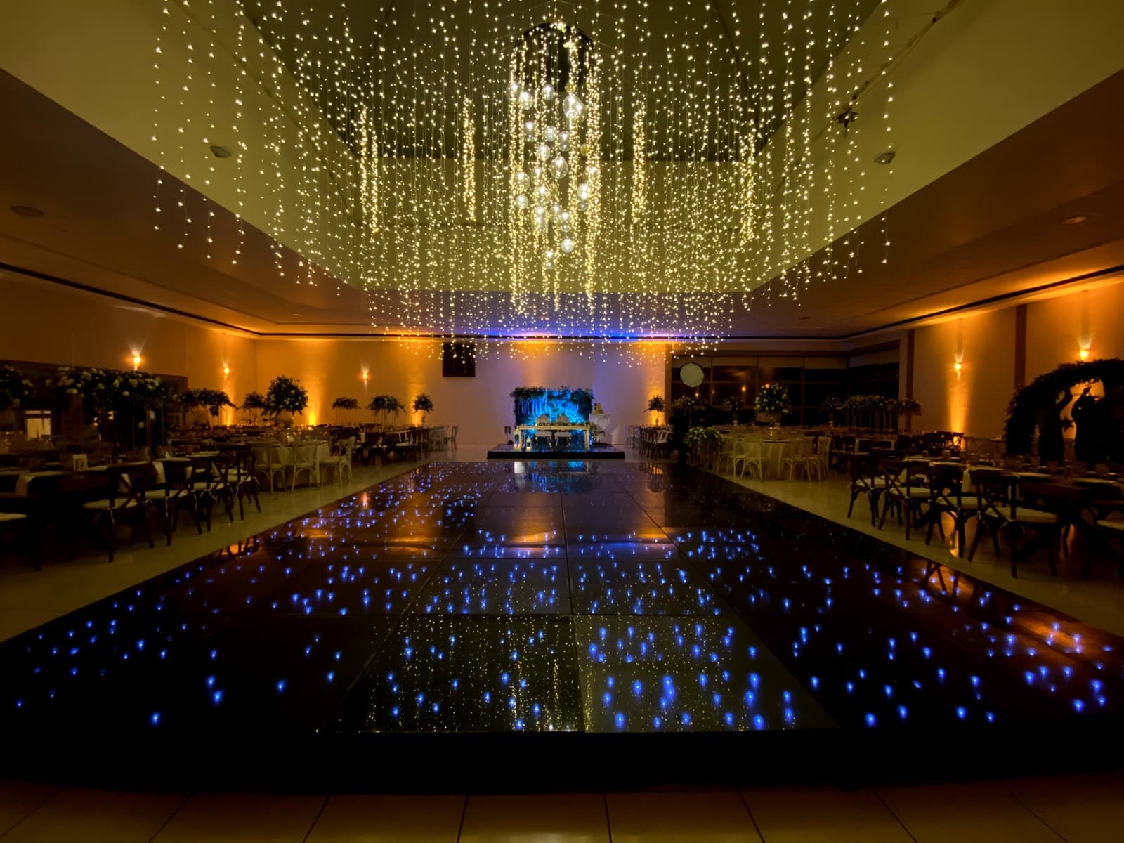 Pista de baile starlight negra reflejando cascada de luces cálidas en salón de eventos