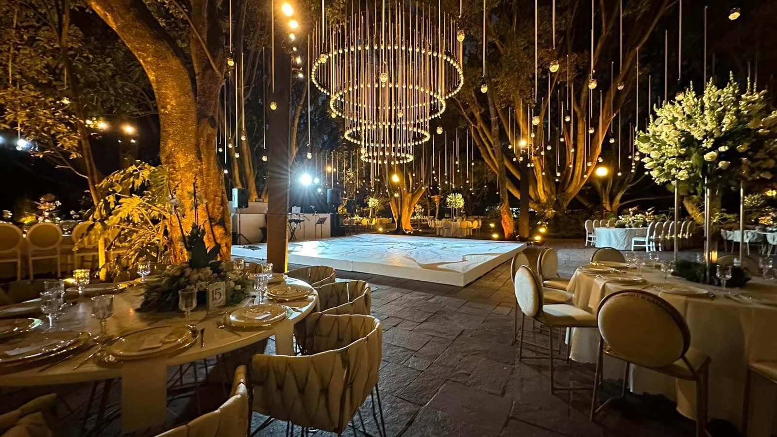 Producción nocturna en jardín con candiles dorados, lluvia de luces y pista iluminada