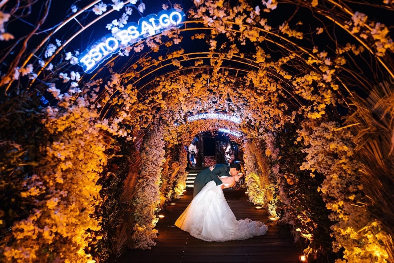 Túnel de flores doradas iluminado con pareja de novios al fondo